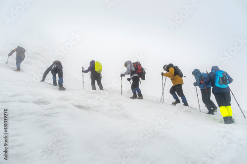 group of alpinist climbing by steep snow slope in snowfall