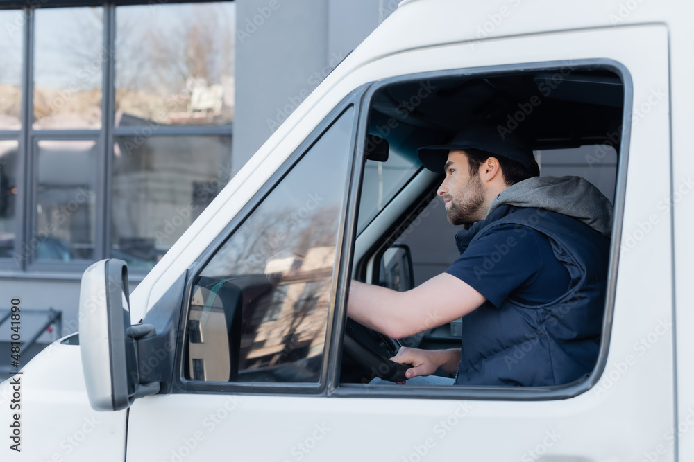 Side view of young courier in uniform driving auto. Side view of young courier in uniform driving auto.