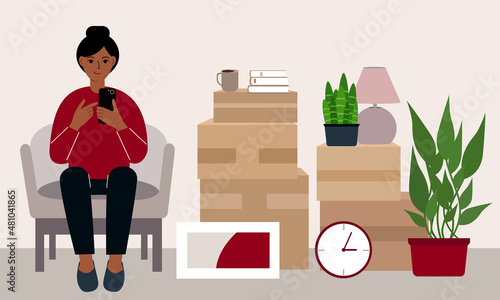 A woman at home with a mobile phone sits in a chair. The concept of online registration of delivery of boxes, goods and assistance in moving.