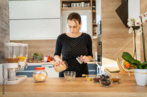One young caucasian woman standing in the kitchen making healthy breakfast front view millennial female adult putting oatmeal oatflakes in the bowl preparing meal real people copy space photo
