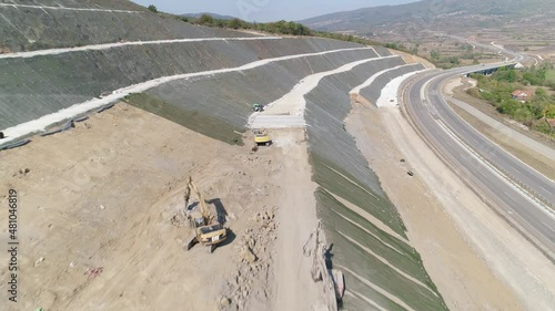 Several industrial machines working on an highway embankment on a sunny day. Construction machines. Aerial drone shot. Roadworks. photo