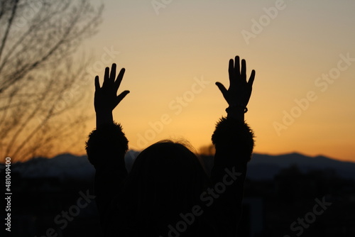 Fototapeta silhouette of a little girl raising her hands at sunset with joy