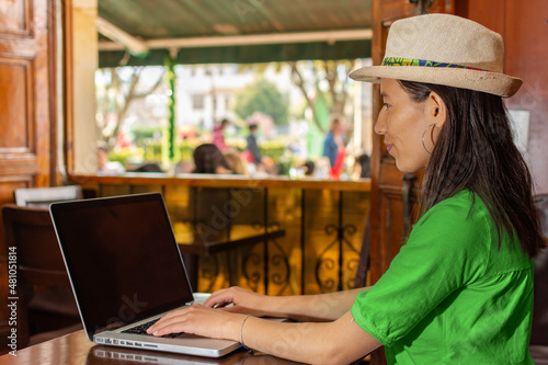 Latin woman wearing a hat and green blouse, sitting in a old coffee shop working on her laptop