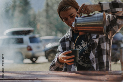 Man sitting at a campsite pouring coffee from a percolator 