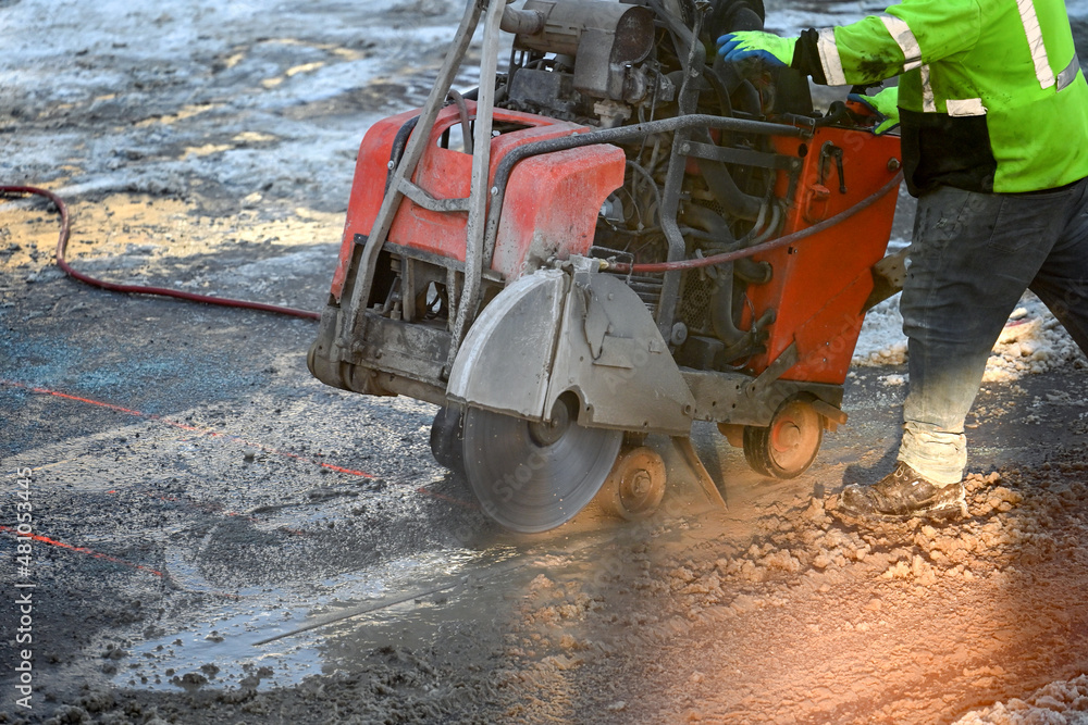 Worker using an asphalt saw cutting machine in winter Worker using an asphalt saw cutting machine in winter