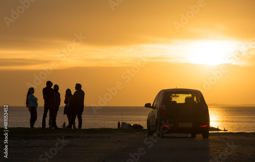 Amigos conversando encuentro en la costa, hora dorada en atardecer con un auto estacionado