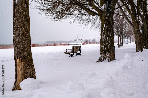 Canvas Print A park bench covered in snow sits on an empty beach beside a boardwalk after a blizzard