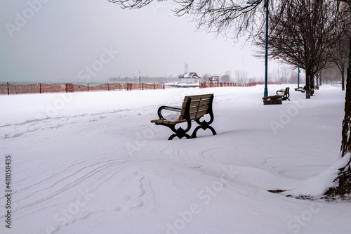 A park bench covered in snow sits on an empty beach beside a boardwalk after a blizzard.  Shot in Toronto's Beaches neighbourhood. © Michael Connor Photo