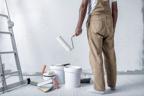 a man paints a white wall with a roller. Repair of the interior. Young male decorator painting a wall in the empty room, concept builder or painter in helmet with paint roller over the empty room