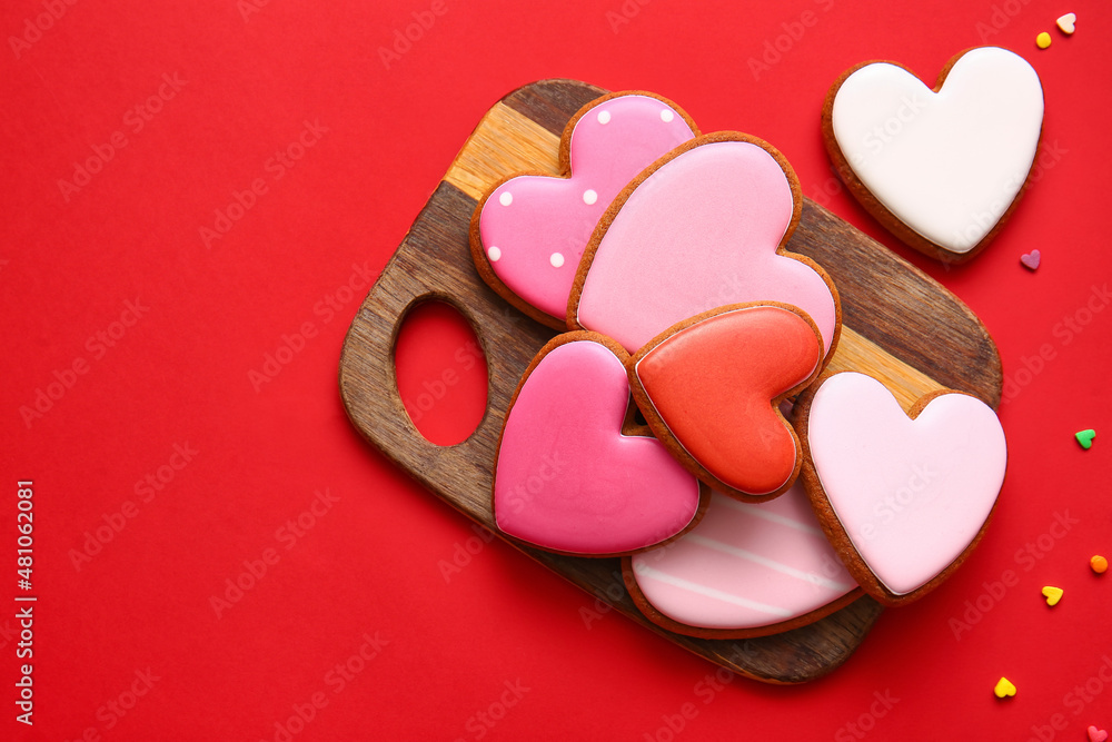 Wooden board with tasty heart shaped cookies on red background Wooden board with tasty heart shaped cookies on red background