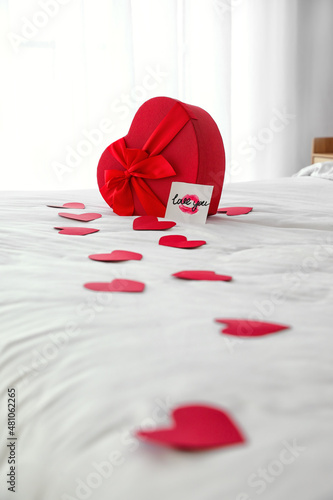Gift for Valentine's Day and red paper hearts on bed