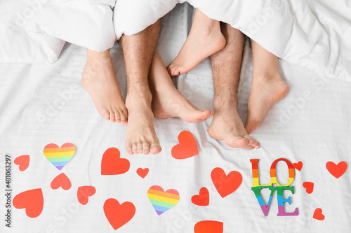 Legs of young man and two women lying in bed covered with paper hearts, top view. Concept of polyamory and LGBT photo