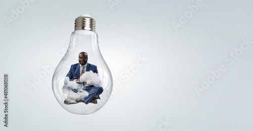 Young black man sitting and meditating inside light bulb © Sergey Nivens