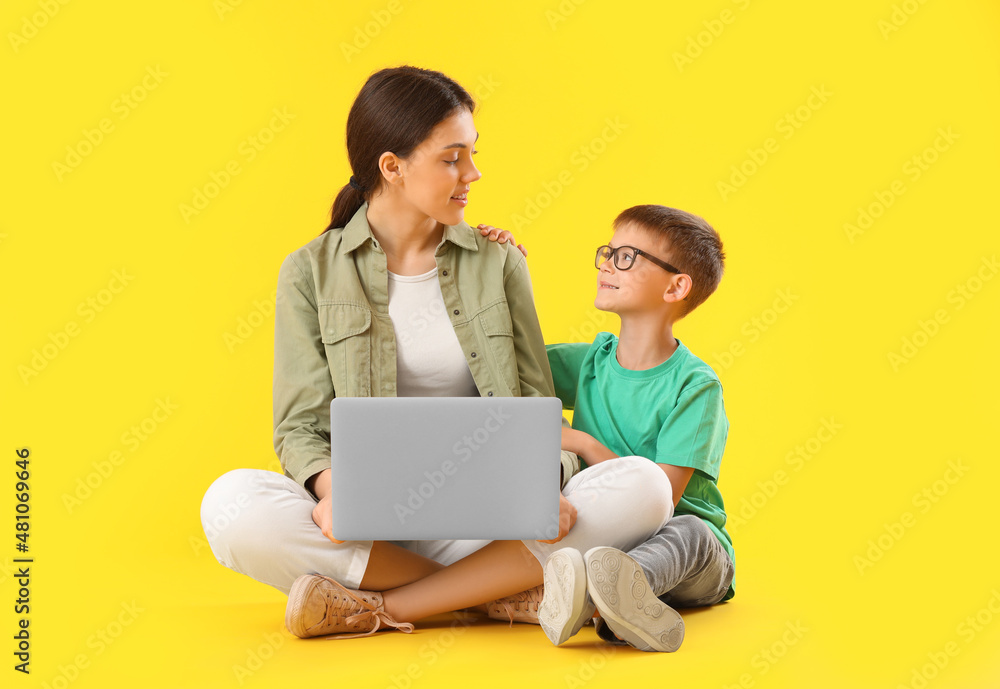 Little boy with his older sister using laptop on yellow background