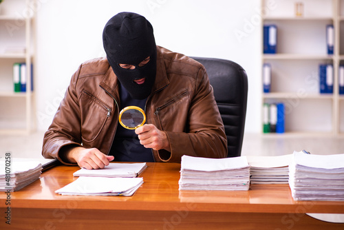 Young man in balaclava stealing information from the office