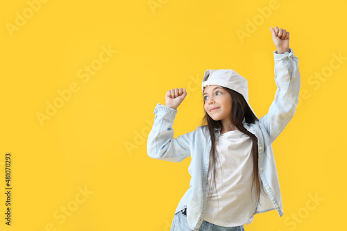 Adorable little girl in cap dancing on yellow background