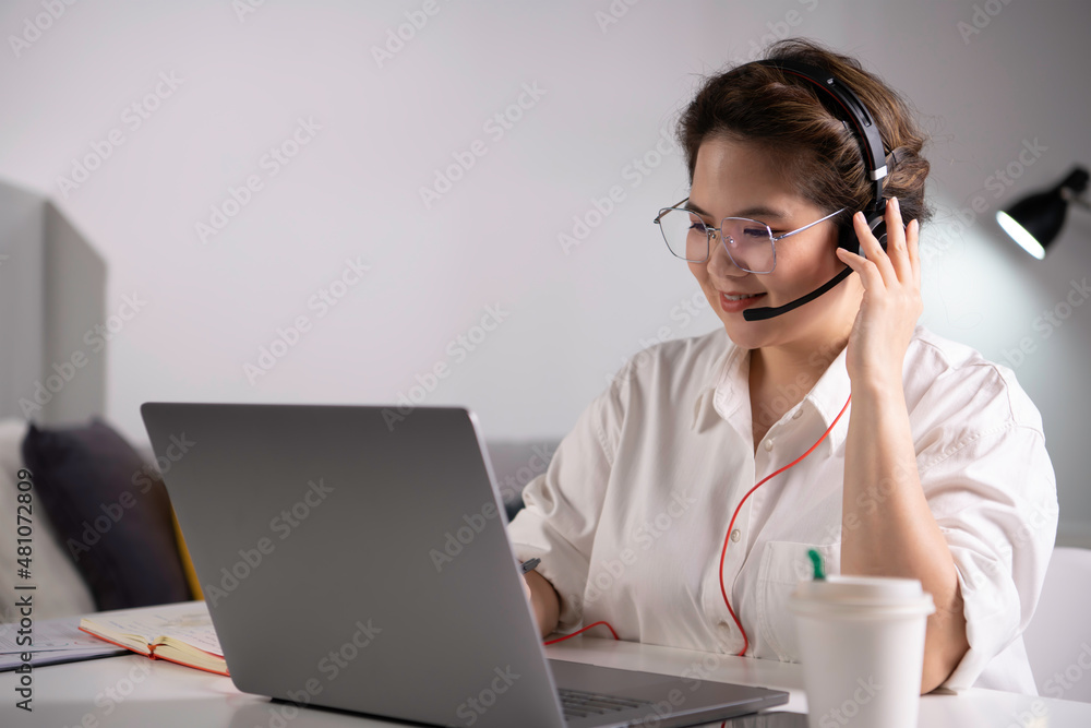 Feeling good happy and positive at work. Young Asian businesswoman wearing headset on video call with clients on laptop. Young Asian woman giving online educational class lecture, consulting customer. Feeling good happy and positive at work. Young Asian businesswoman wearing headset on video call with clients on laptop. Young Asian woman giving online educational class lecture, consulting customer.