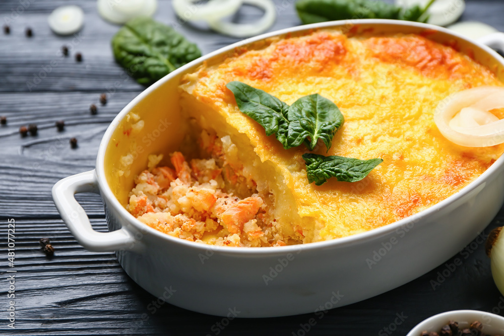 Baking dish with tasty English fish pie on black wooden background Baking dish with tasty English fish pie on black wooden background