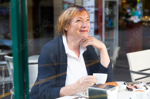 Portrait of smiling elderly woman drinking coffee in modern city cafe