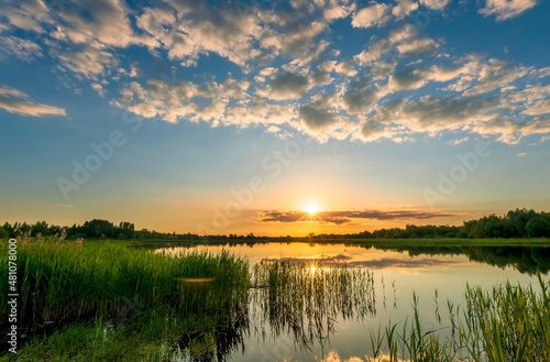 Amazing view at scenic landscape on a beautiful lake and colorful sunset with reflection on water surface among green reeds and glow on a background  spring season landscape