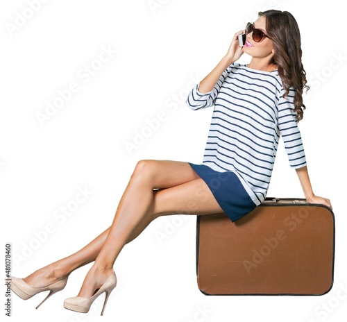 Beautiful woman sitting on suitcase and talking on phone