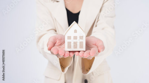 Young beautiful woman in suit holding small model house over white background studio