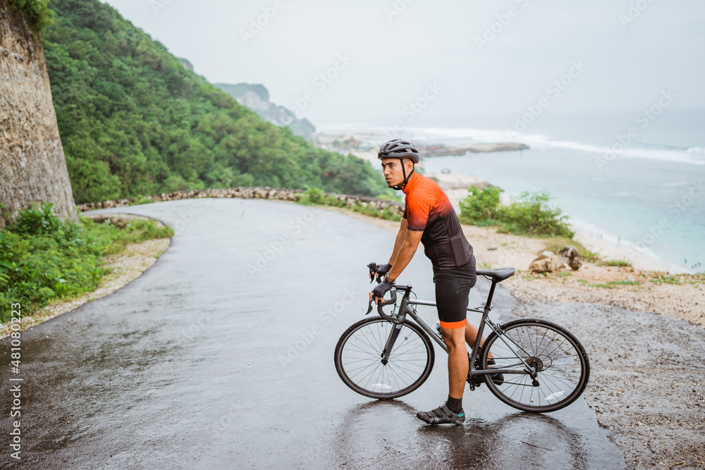 male asian cyclist with red and black jersey standing on his bike male asian cyclist with red and black jersey standing on his bike