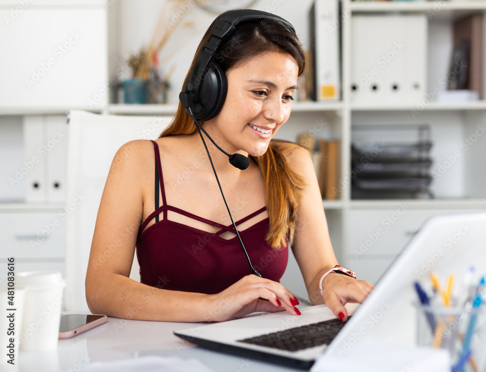 Naklejka premium Young woman call centre operator with headphones working in modern office