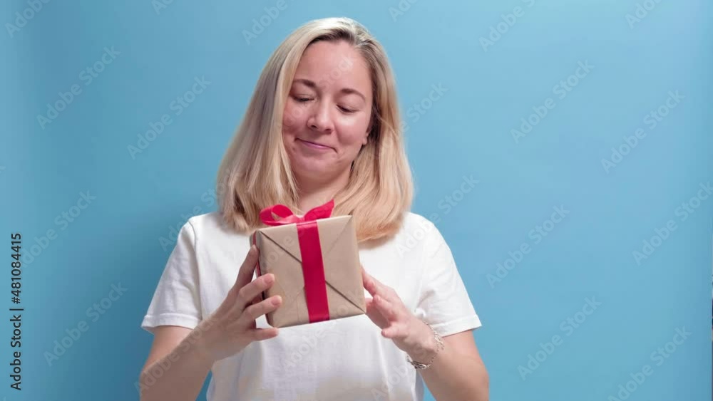 4k.Young smiling woman holding gift box and gives it by hands to camera on blue background. Girl is happy with present. Holiday concept of Valentines Day, womens day, Mothers day, 8 March, Birthday 4k.Young smiling woman holding gift box and gives it by hands to camera on blue background. Girl is happy with present. Holiday concept of Valentines Day, womens day, Mothers day, 8 March, Birthday