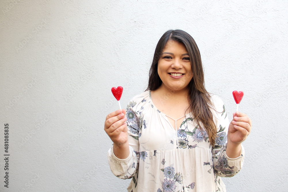 Latin adult woman with red heart-shaped lollipops to show her enthusiasm for the arrival of February and celebrate and show her affection on Valentine's Day of Love and Friendship with her family, fri