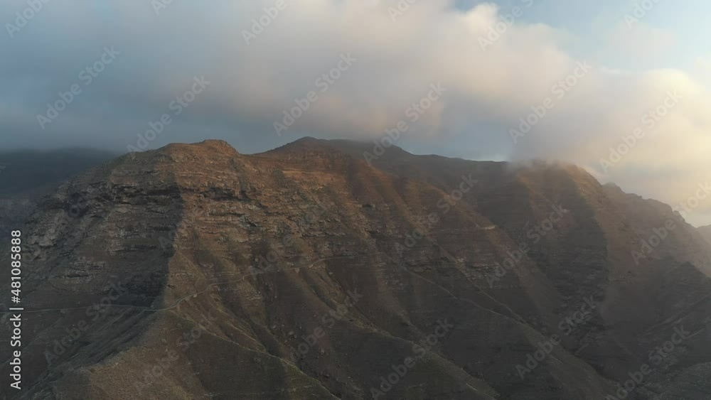 Aerial View Of Rugged Canary Islands Coastline With Pan Right Reveal Of Golden Yellow Sunset Through Clouds Out To See. Slow Pan Right Aerial View Of Rugged Canary Islands Coastline With Pan Right Reveal Of Golden Yellow Sunset Through Clouds Out To See. Slow Pan Right