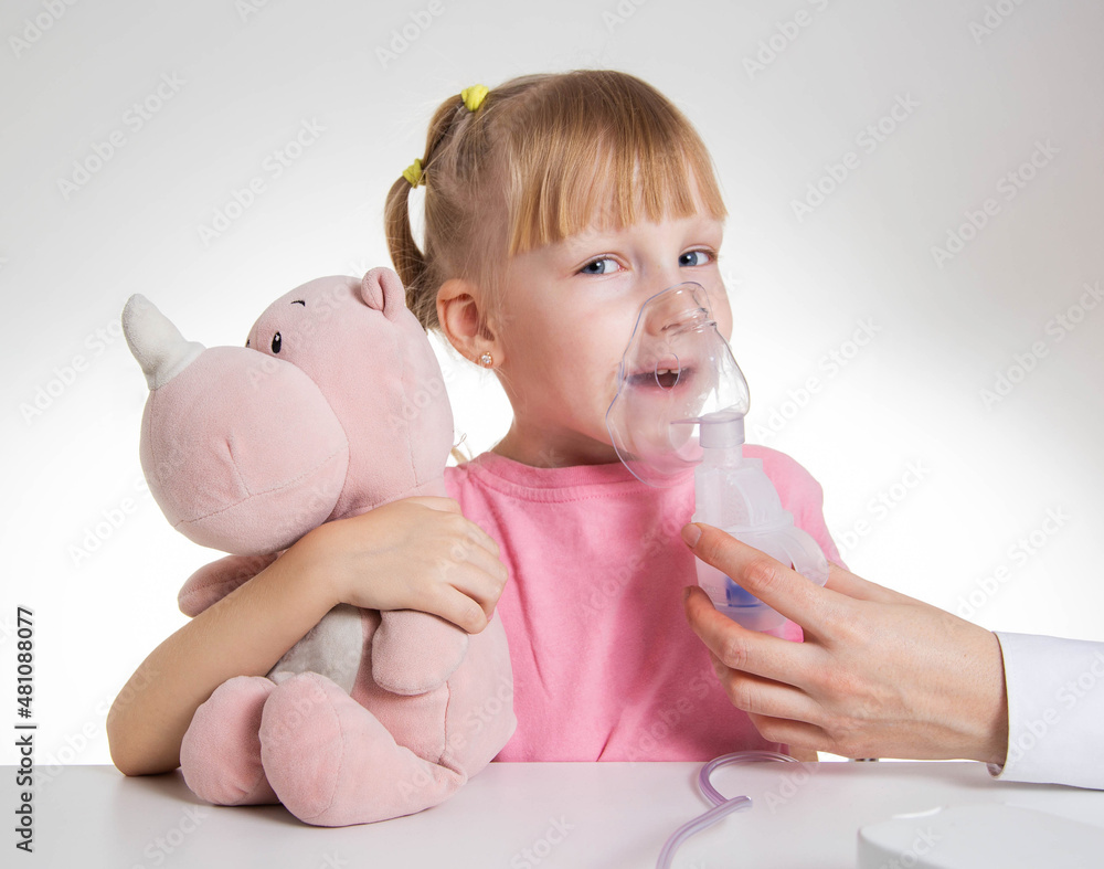 A little girl 5 years old in a pink T-shirt breathes into a nebulizer for lung disease. Treatment of bronchitis with inhalation, pharyngitis A little girl 5 years old in a pink T-shirt breathes into a nebulizer for lung disease. Treatment of bronchitis with inhalation, pharyngitis