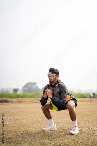 Young Indian sports man doing squats in the field. Sports and healthy lifestyle concept.
