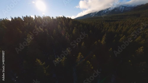 FPV drone shot captured in Slovenia in Pokljuka forest with surrounding nature and mountains at golden hour at sunset with fast and cinematic movement from over the clouds to the village photo