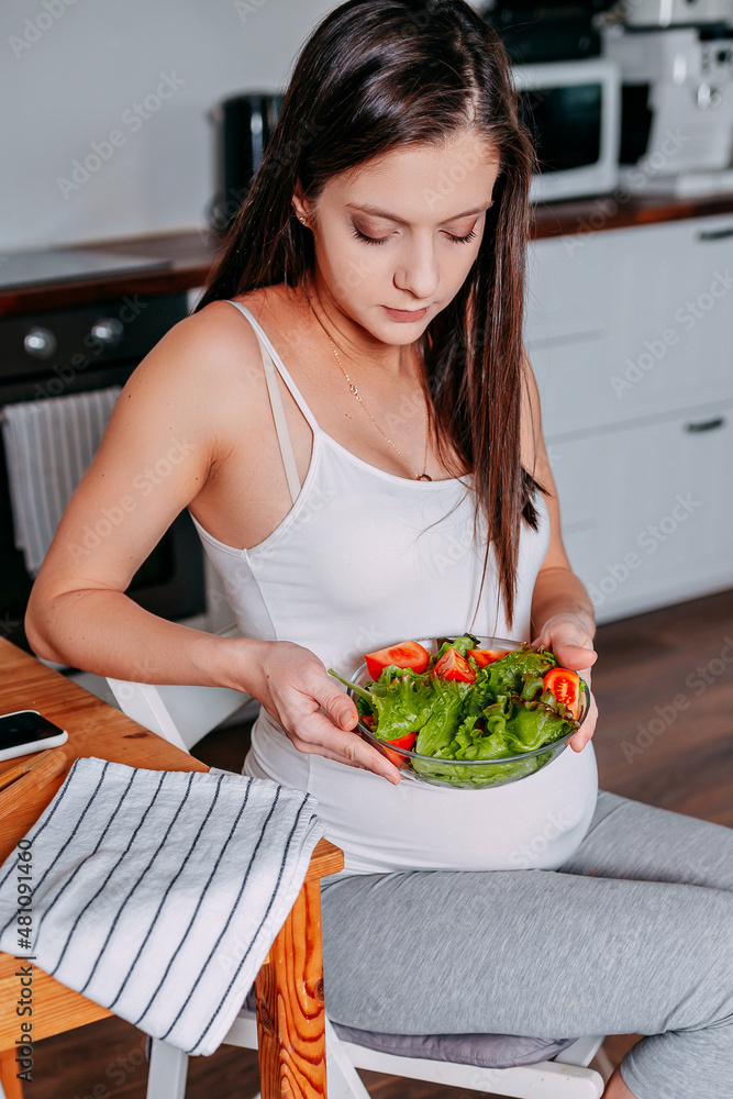 Pregnant eating healthy food. Pregnant woman in the kitchen. Pregnant eats green salad. Pregnant on diet.