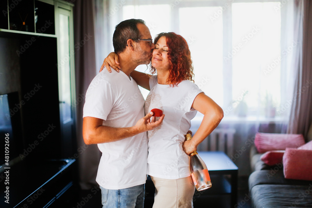 Fototapeta premium cute middle aged european couple in apartment, man proposes to woman. Lifestyle in a real interior with a dog Cavalier King Charles Spaniel