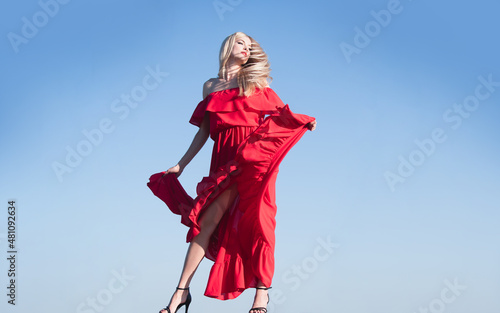 Woman in red dress movement on sky. Fashion outdoor photo of gorgeous sensual woman in elegant dress clothes. Beauty and fashion girl. Carefree women outside.