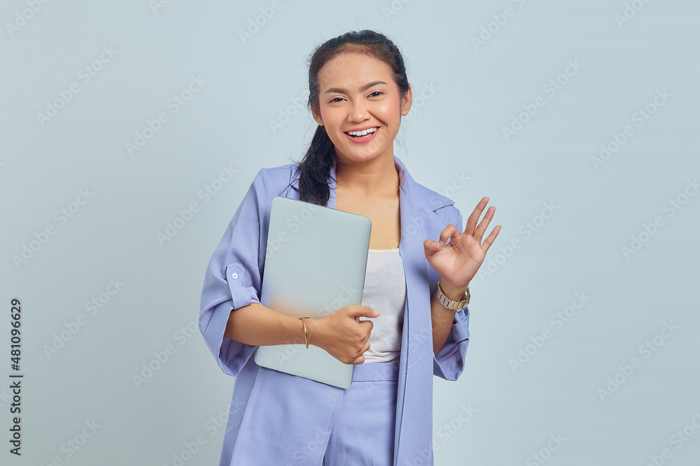 Portrait of beautiful Asian woman holding laptop smiling and showing ok sign over white background Portrait of beautiful Asian woman holding laptop smiling and showing ok sign over white background