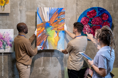 Fotografie Two young men hanging abstract painting on wall while preparing for presentation