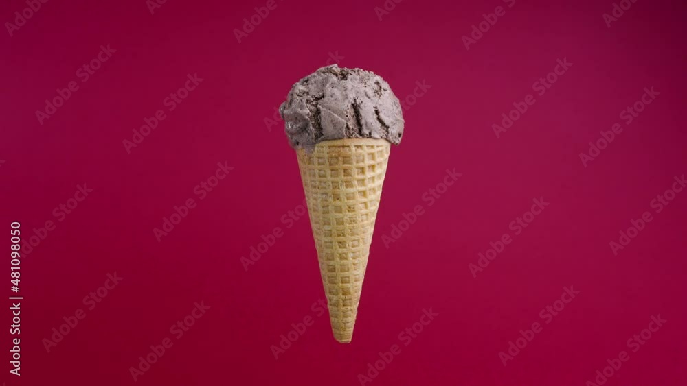 Rotating chocolate ice cream ball in waffle cone on red background. Soft cream cone close-up. Gelato icecream scoop in waffle cone over colorful background Rotating chocolate ice cream ball in waffle cone on red background. Soft cream cone close-up. Gelato icecream scoop in waffle cone over colorful background