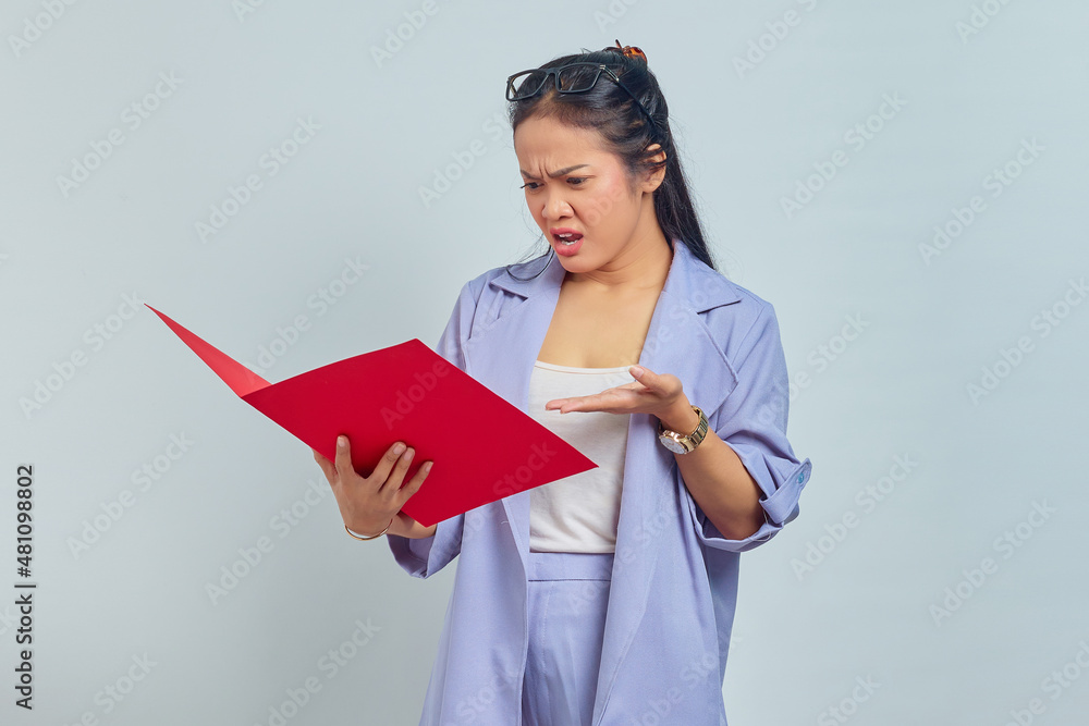 Portrait of angry young Asian business woman in suit standing pointing at document folder with palms isolated on purple background Portrait of angry young Asian business woman in suit standing pointing at document folder with palms isolated on purple background