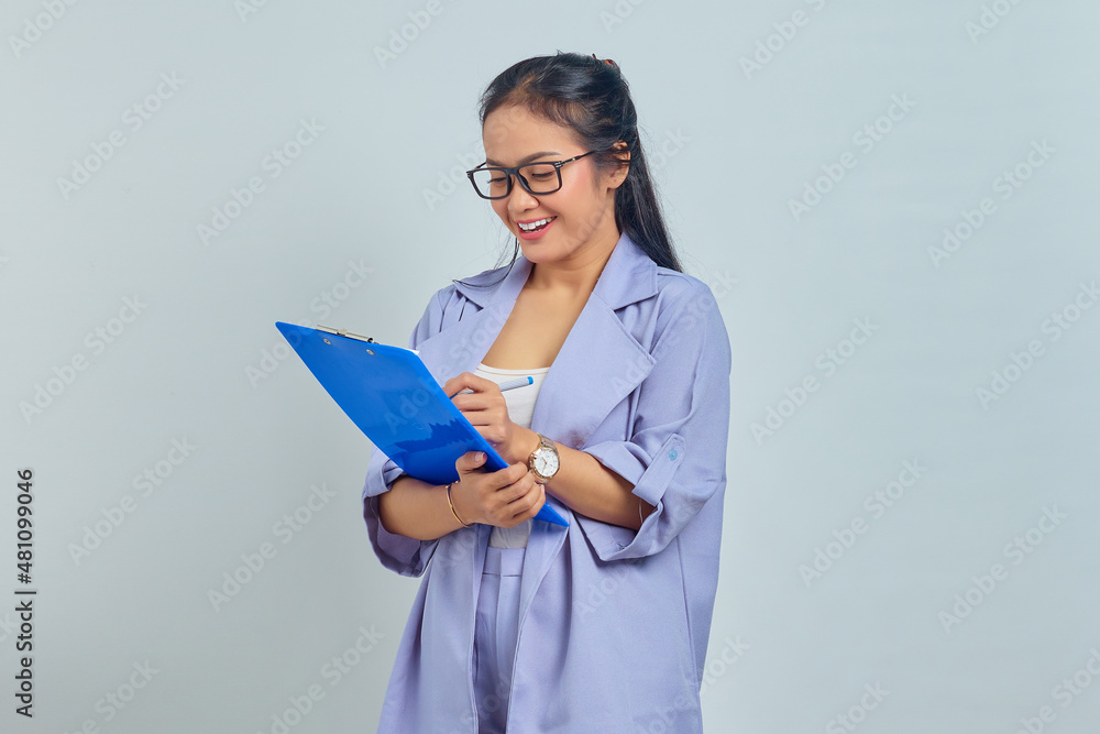 Portrait of beautiful young Asian business woman in suit standing holding document folder with smiling face on purple background Portrait of beautiful young Asian business woman in suit standing holding document folder with smiling face on purple background
