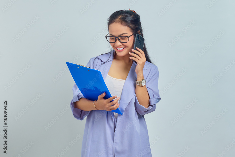 Portrait of cheerful young Asian woman laughing while talking on mobile phone with friends about something funny while holding document folder isolated on purple background Portrait of cheerful young Asian woman laughing while talking on mobile phone with friends about something funny while holding document folder isolated on purple background