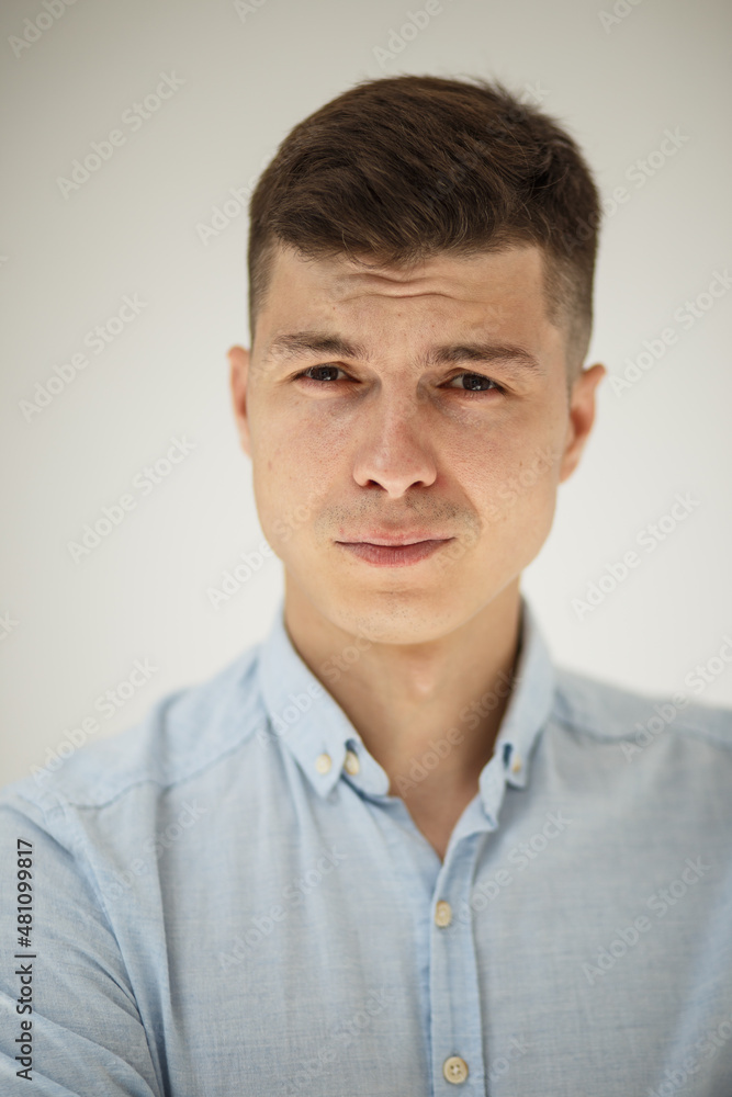 teen guy looking into the frame surprised can't believe raised eyebrows and sincerely smiling on a white background in a blue shirt teen guy looking into the frame surprised can't believe raised eyebrows and sincerely smiling on a white background in a blue shirt