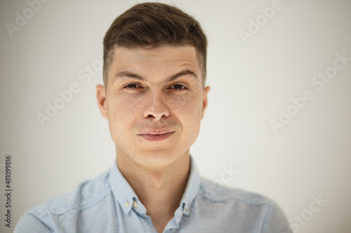 teen guy looking into the frame surprised can't believe raised eyebrows and sincerely smiling with teeth on a white background in blue shirt