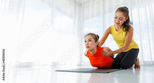 Asian coach supporting woman during yoga session