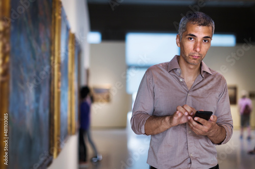 Man is looking at the exposition with phone in the museum.