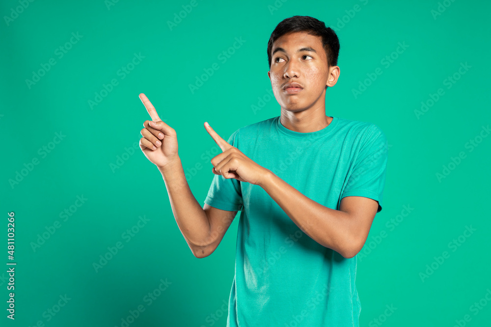 Portrait of a happy young man in white t-shirt pointing fingers away at copy space isolated over green background Portrait of a happy young man in white t-shirt pointing fingers away at copy space isolated over green background