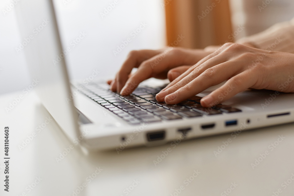 Indoor shot of faceless unknown anonymous woman typing text on keyboard on laptop, programming, doing her online work on portable notebook.