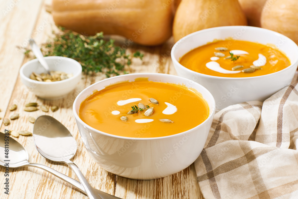 Delicious pumpkin soup in bowls with cream sauce on a white wooden table, selective focus. Delicious pumpkin soup in bowls with cream sauce on a white wooden table, selective focus.